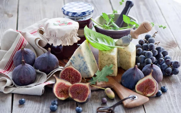 HD desktop wallpaper featuring a still life of fresh grapes, figs, assorted cheeses, and jars of jam on a rustic wooden table.