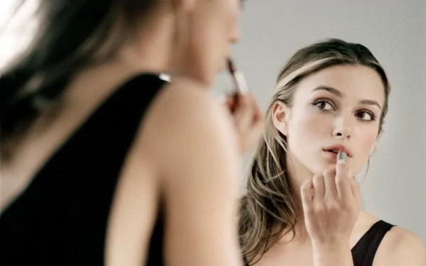 HD desktop wallpaper featuring Keira Knightley applying lipstick while looking into a mirror, set against a soft background.