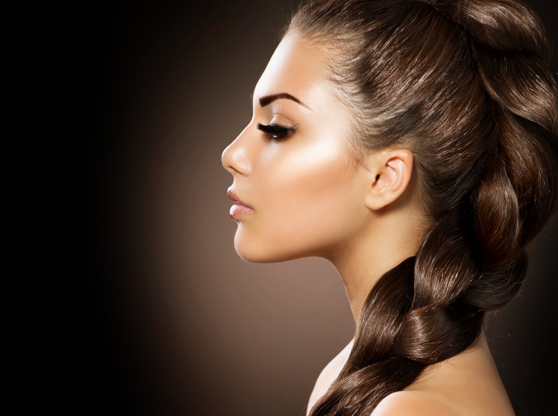 Profile of a brunette woman with braided hair against a dark background, captured in high-resolution 4K Ultra HD, highlighting smooth skin and defined features.
