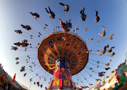 Vibrant carnival swing ride with people soaring through the colorful amusement park sky, captured in a dynamic HD desktop wallpaper.