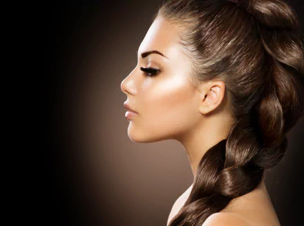 Profile of a brunette woman with braided hair against a dark background, captured in high-resolution 4K Ultra HD, highlighting smooth skin and defined features.
