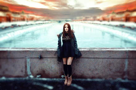 HD desktop wallpaper featuring a brunette woman model standing outdoors by a blurred waterfront with vibrant colors and a dramatic sky.