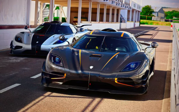 A stunning HD desktop wallpaper featuring two Koenigsegg supercars, including the sleek Koenigsegg Agera, parked on a racetrack under sunlight.