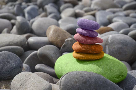 A serene arrangement of colorful pebbles stacked on a green stone, set against a backdrop of smooth gray stones, creating a calm, zen-like atmosphere in this vibrant 4K Ultra HD wallpaper.