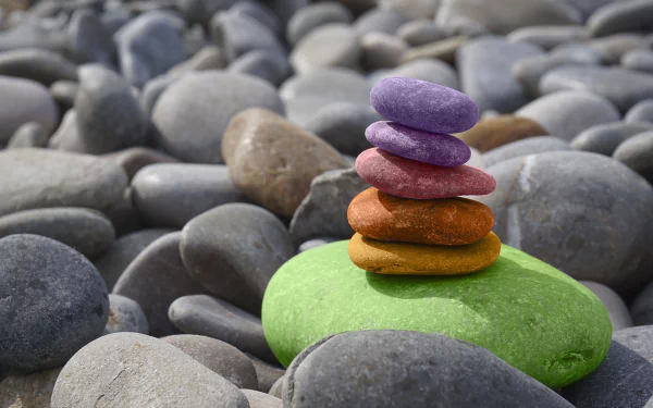 A serene arrangement of colorful pebbles stacked on a green stone, set against a backdrop of smooth gray stones, creating a calm, zen-like atmosphere in this vibrant 4K Ultra HD wallpaper.