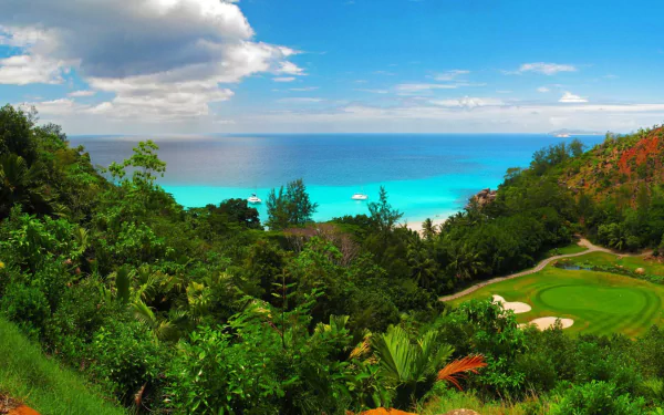 A vibrant coastline view featuring a lush golf course, with the deep blue ocean and horizon in the background, framed by greenery and dotted with distant boats.