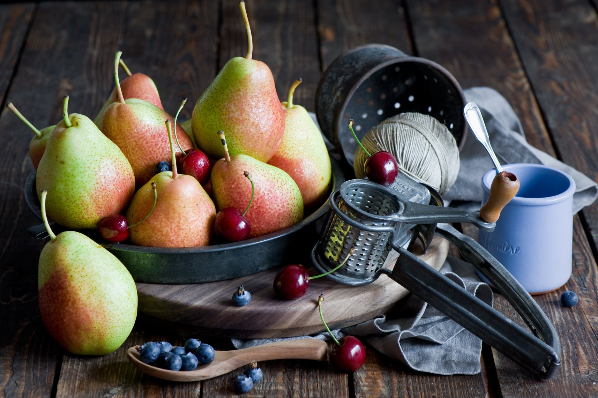 A still life HD desktop wallpaper featuring fresh pears, blueberries, and cherries arranged with vintage kitchen tools on a rustic wooden surface.