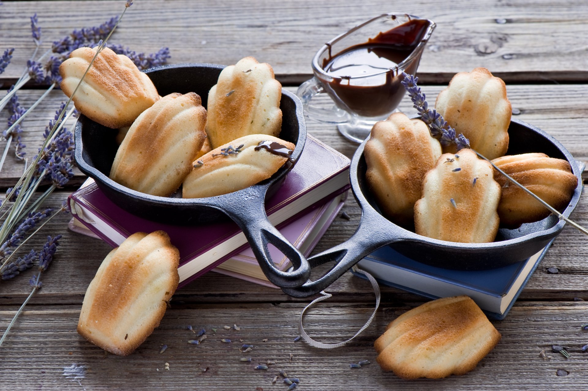 HD PC desktop wallpaper still life: madeleines in cast-iron pans with chocolate sauce and lavender sprigs arranged on a rustic wooden table.