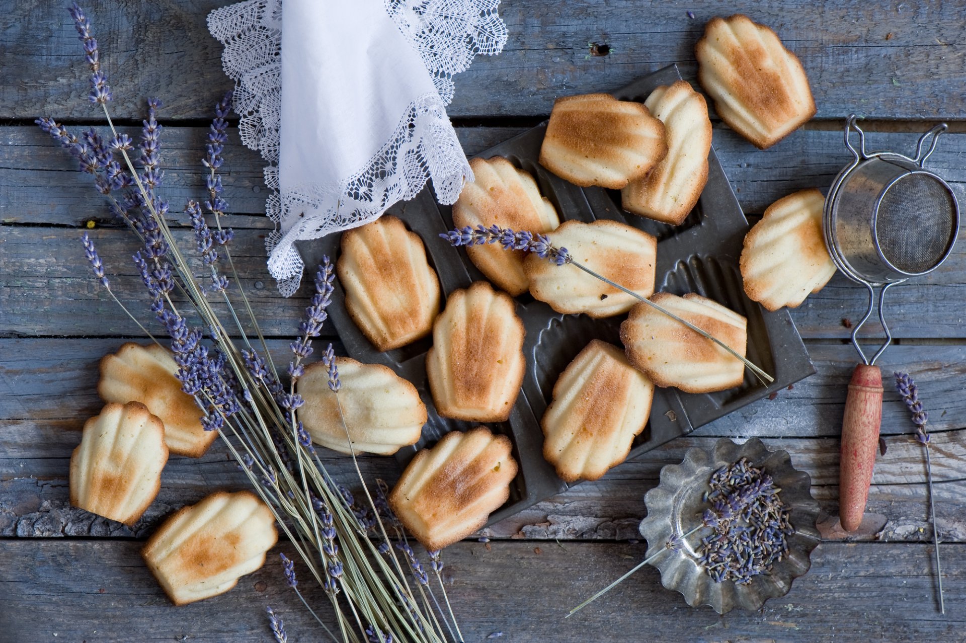 HD still life PC wallpaper featuring golden madeleine cookies, sprigs of lavender, and vintage kitchen tools on a rustic wooden surface.