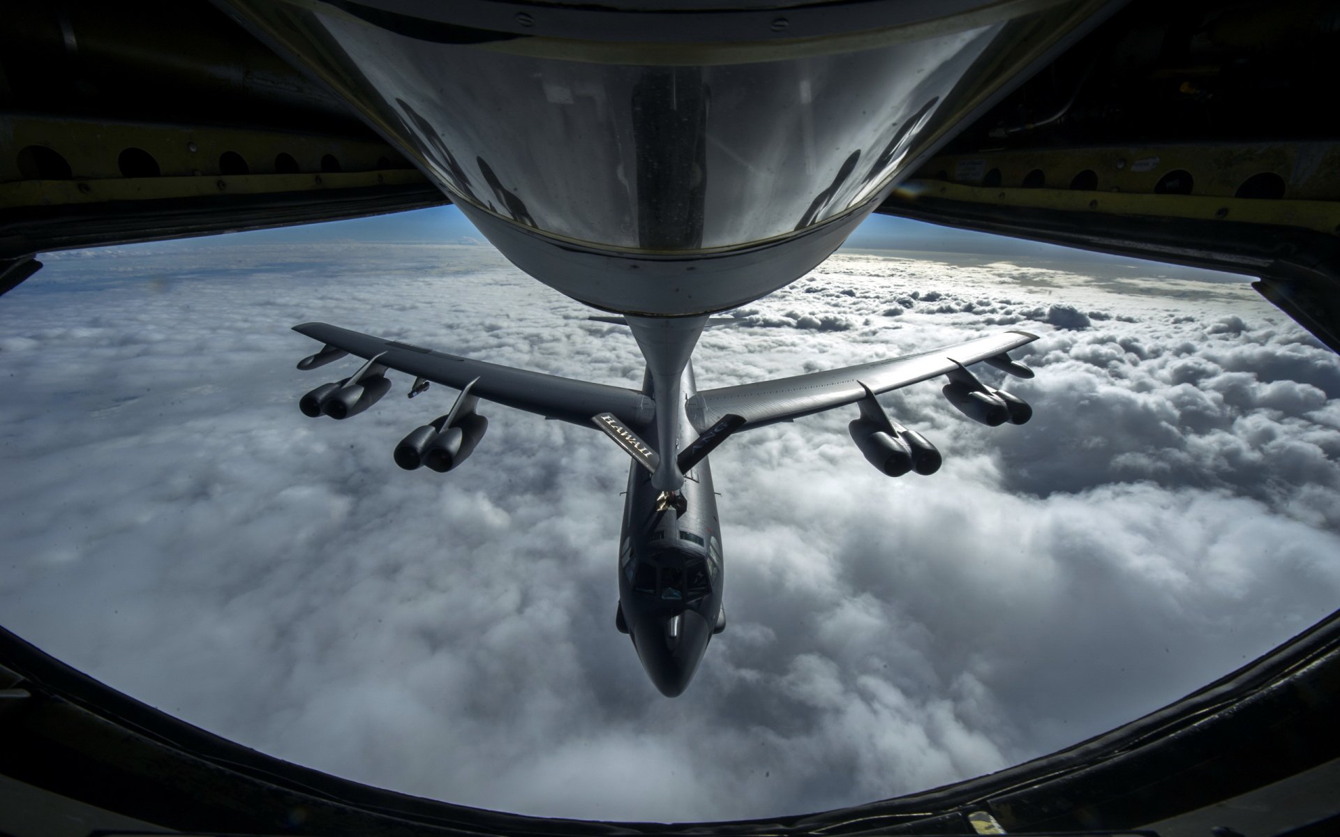 A dramatic view of a Boeing B-52 Stratofortress bomber flying above the clouds, captured from the cockpit, showcasing its military prowess and aerial dominance.
