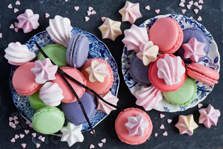 A vibrant still life featuring colorful meringue kisses and macarons arranged on decorative plates, complemented by delicate heart-shaped sprinkles, creating a delightful pastry display.