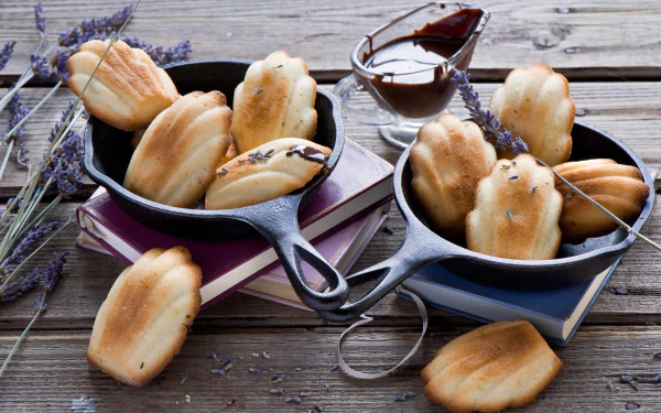HD PC desktop wallpaper still life: madeleines in cast-iron pans with chocolate sauce and lavender sprigs arranged on a rustic wooden table.