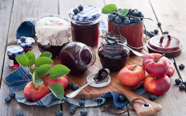 Still life of jars filled with blueberry jam, fresh blueberries, and apples arranged on a wooden surface, captured in vibrant 4K Ultra HD detail for a PC desktop background.