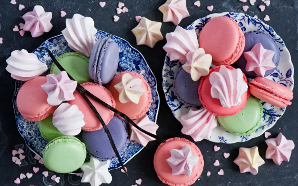 A vibrant still life featuring colorful meringue kisses and macarons arranged on decorative plates, complemented by delicate heart-shaped sprinkles, creating a delightful pastry display.