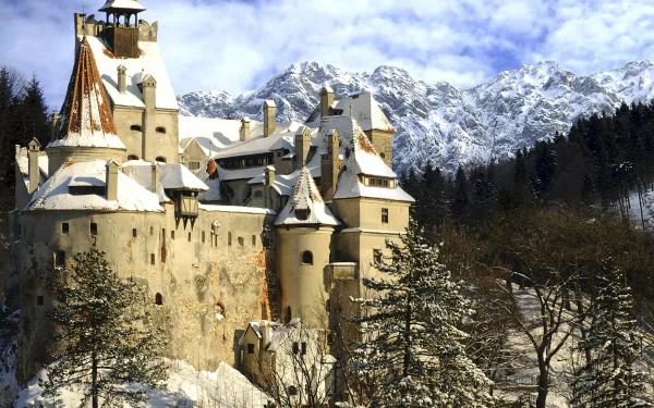 Bran Castle stands majestically against a snowy mountain backdrop, captured in stunning 4K Ultra HD as a striking man-made architectural landmark.