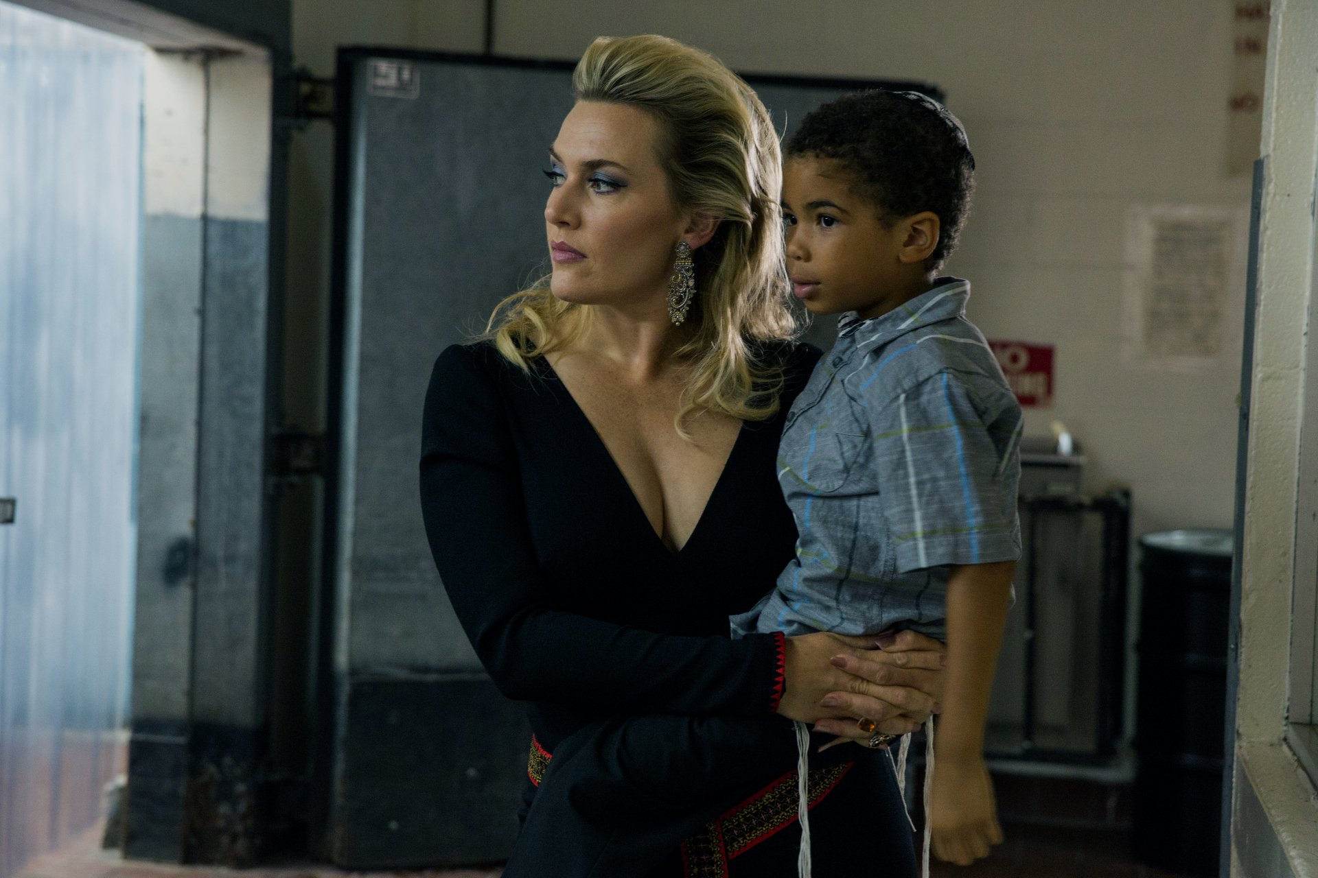 Kate Winslet, portrayed in a scene from the movie *Triple 9*, holds a young boy as they navigate a tense environment. This image serves as a striking 4K Ultra HD wallpaper.