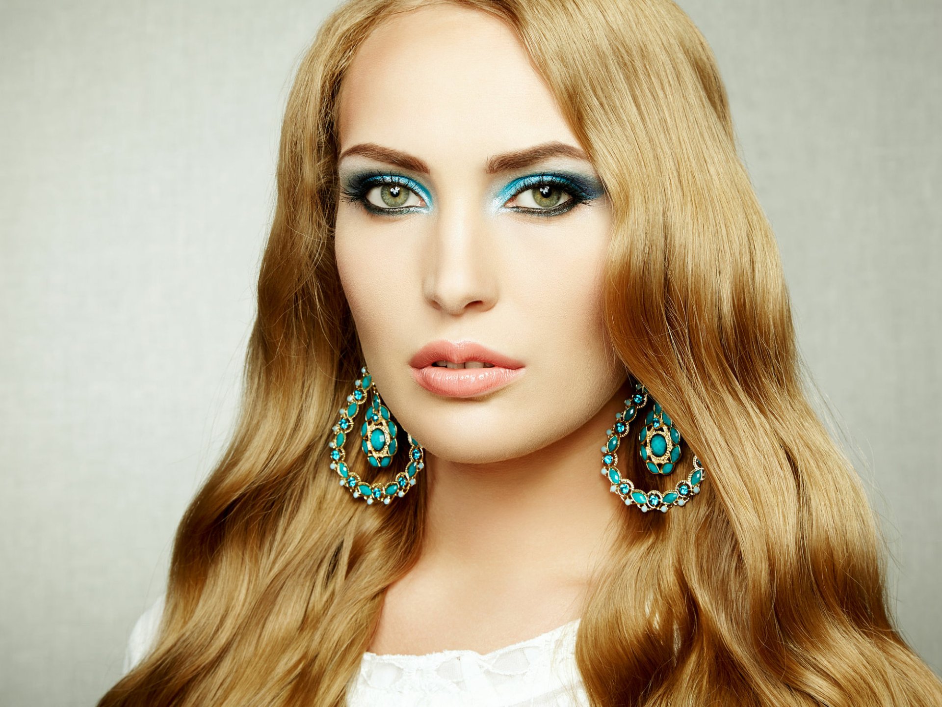 HD desktop wallpaper featuring a blonde woman with striking green eyes, wearing ornate blue and gold earrings.