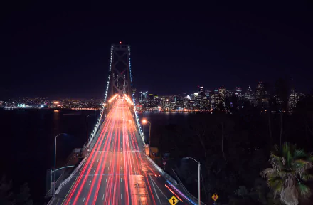 A stunning time-lapse view of San Francisco's Bay Bridge at night, showcasing vibrant light trails over the road, with the city skyline illuminated in the background.