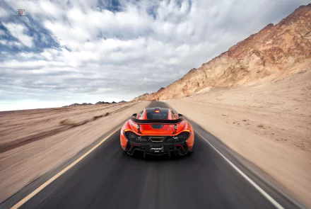 Orange McLaren P1 supercar driving on a desert road with rocky hills under a cloudy sky, captured in a 4K Ultra HD PC desktop wallpaper.
