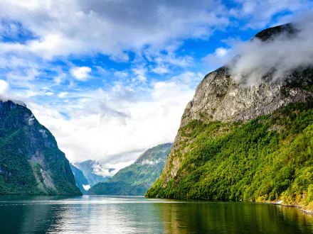 HD PC desktop wallpaper: serene nature fjord with glassy water flanked by steep green mountains beneath a partly cloudy blue sky.