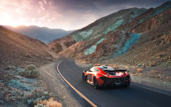 A stunning McLaren P1 supercar in vibrant orange, navigating a scenic winding road through mountainous terrain, with a breathtaking sunset illuminating the landscape.