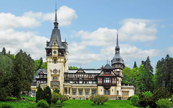 HD PC desktop wallpaper featuring the man-made Peles Castle surrounded by lush greenery under a partly cloudy sky.