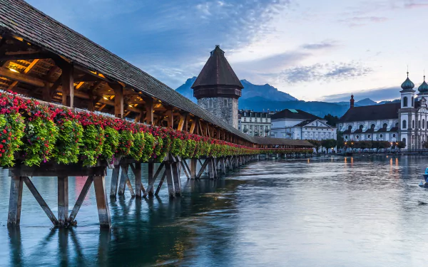 HD PC desktop wallpaper and background: man-made Chapel Bridge (Kapellbrücke) spanning Lucerne's Reuss River at dusk, flower-lined wooden walkway with city and mountain backdrop.