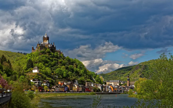 Scenic view of the historic Cochem castle on a hill overlooking a lake and city in Germany under a dramatic cloudy sky.