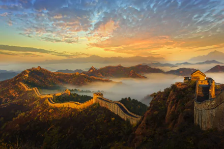A breathtaking HD wallpaper of the Great Wall of China stretching across a mountainous landscape under a colorful sunset sky, with layers of mist adding a magical touch to the horizon.