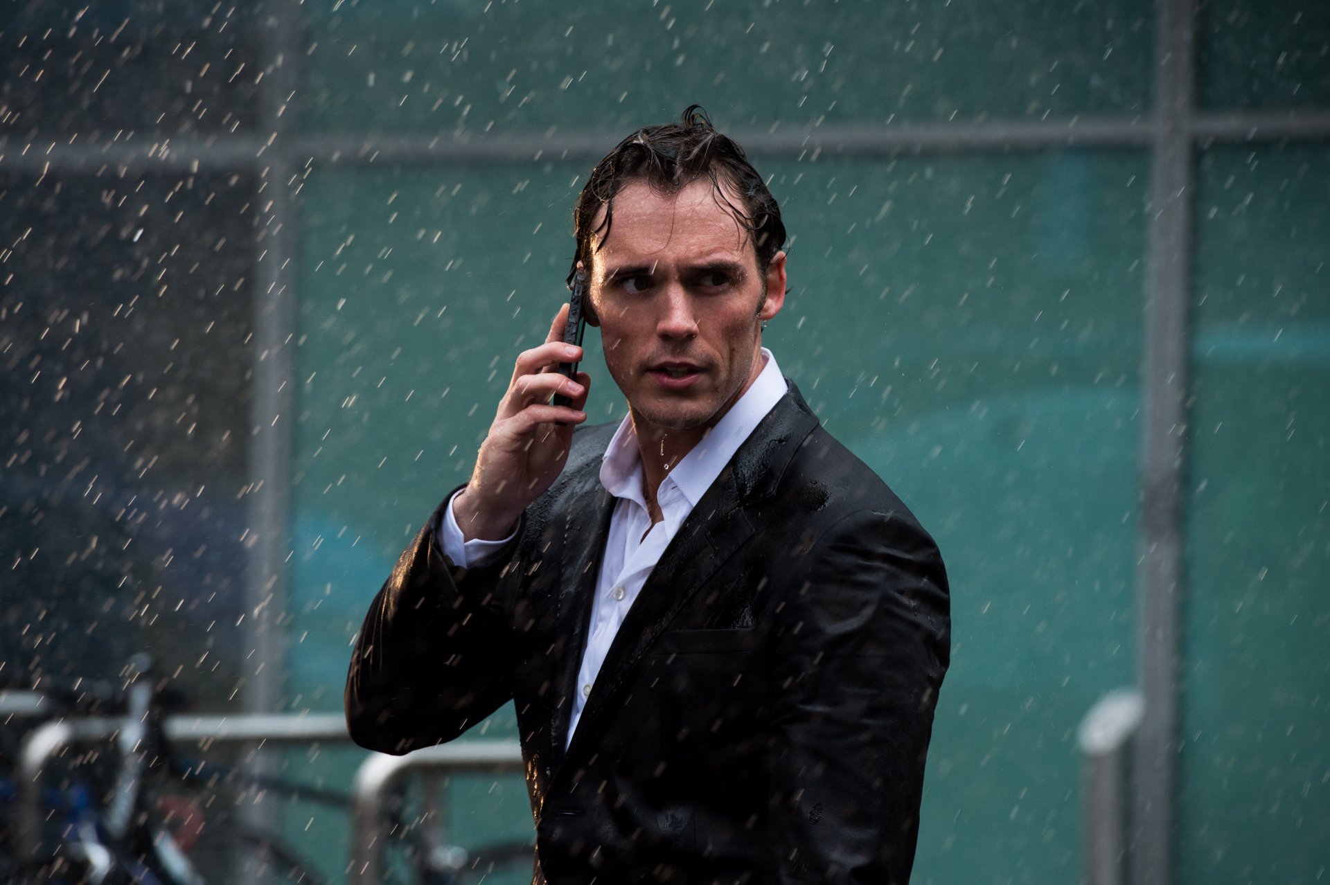 Sam Claflin in a scene from the movie Me Before You, captured in a 4K Ultra HD PC desktop wallpaper showcasing him in a rain-soaked suit talking on the phone.