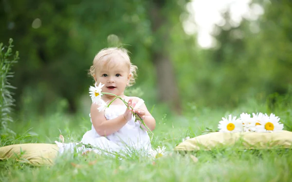 A smiling child sits on grass holding a chamomile flower, surrounded by nature, captured in a bright, serene mood for an HD photography desktop wallpaper.