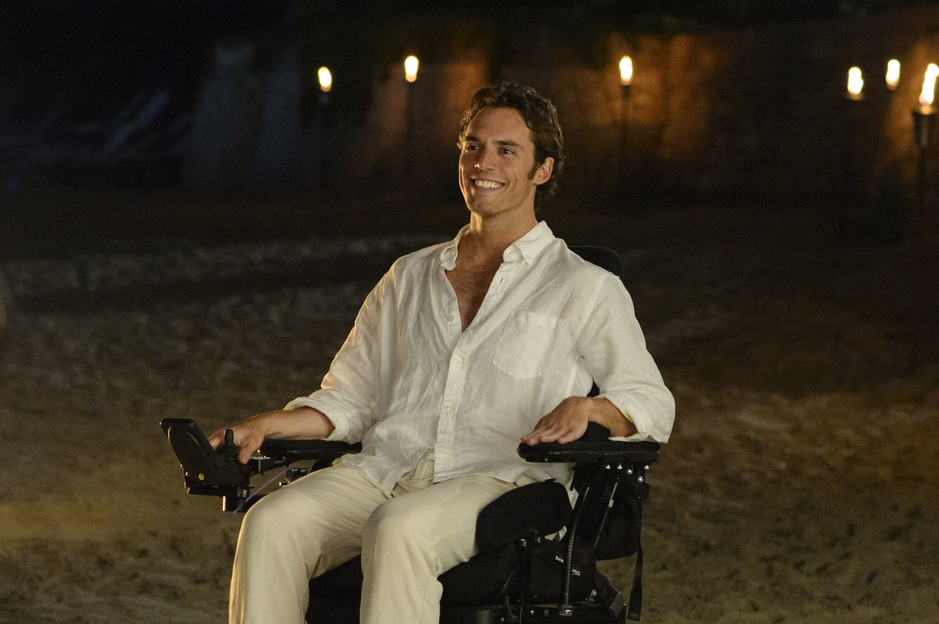 Sam Claflin in a scene from the movie Me Before You, smiling while seated in a wheelchair, featured in an HD PC desktop wallpaper.