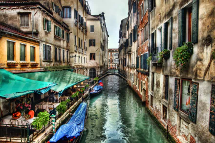 A scenic view of a canal in Venice, Italy, featuring charming buildings and outdoor seating at a restaurant, presented in vibrant HDR for a stunning desktop wallpaper.