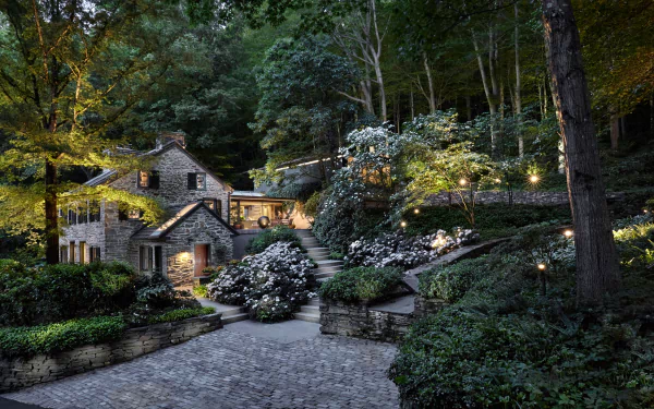 A charming house nestled among lush greenery in Yorkshire, England, features beautiful landscaping and warm lighting, creating a serene and inviting atmosphere.