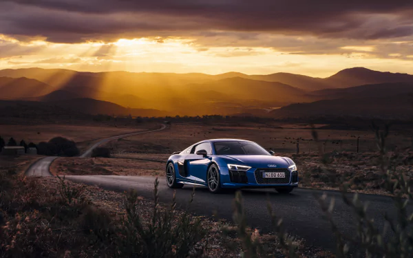 A stunning Audi R8 V10 parked on a scenic road, illuminated by dramatic sunset rays. This 4K Ultra HD background showcases the elegance of this supercar against a rugged landscape.
