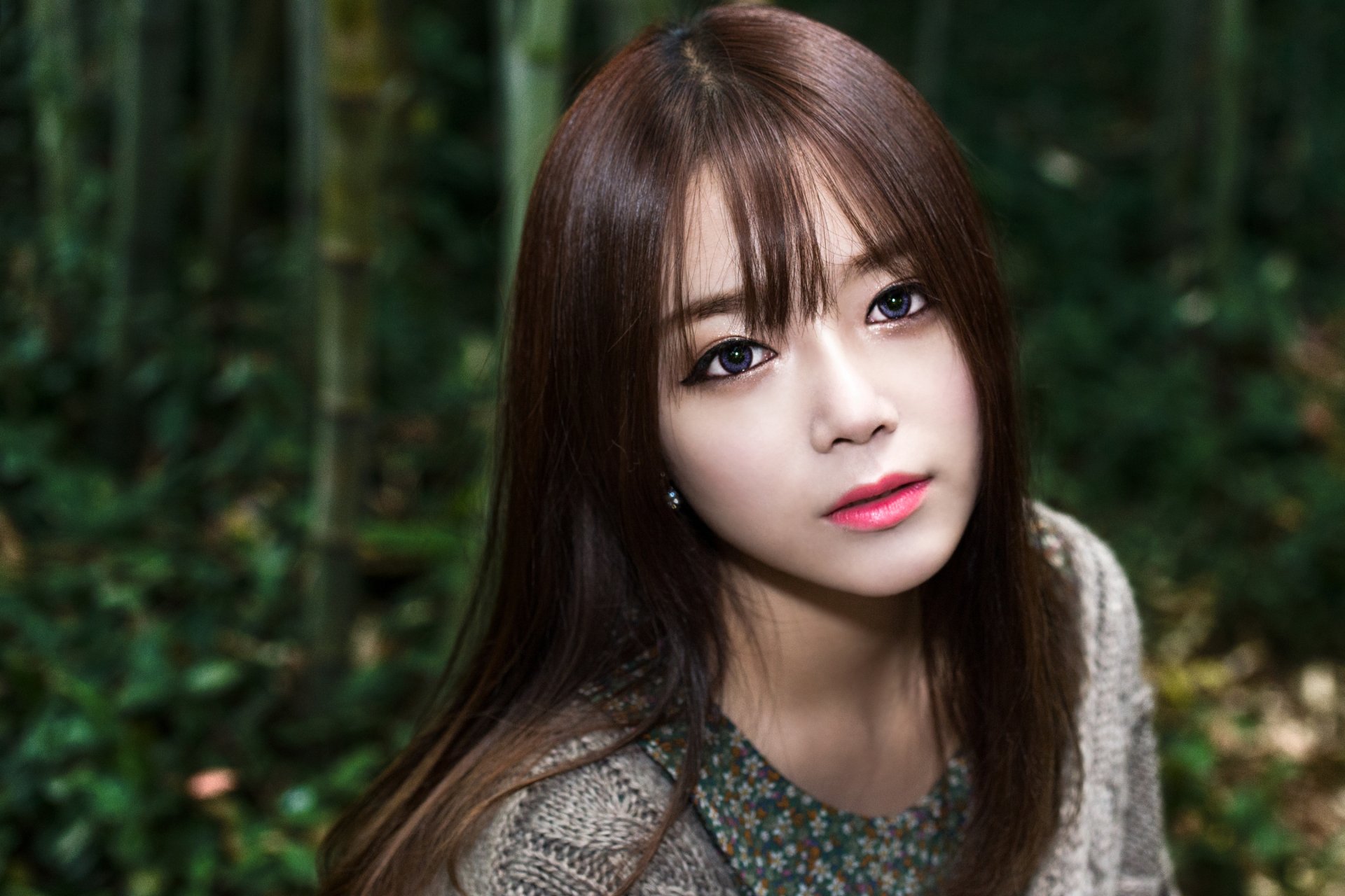 A brunette woman with striking purple eyes gazes thoughtfully at the camera, set against a lush green background, creating a captivating HD wallpaper.