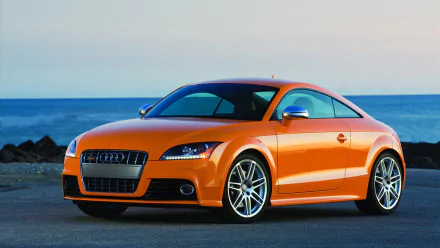 HD desktop wallpaper featuring an orange Audi TT car parked near the coast with a clear sky and ocean in the background.