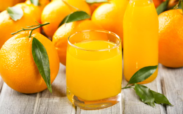A refreshing glass of orange juice surrounded by ripe oranges and green leaves, captured in vibrant color, designed as a 4K Ultra HD desktop wallpaper.