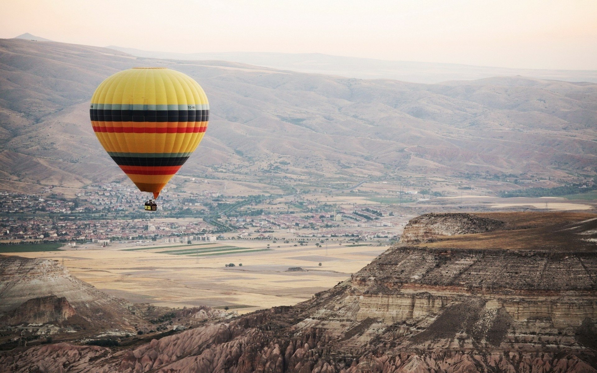 HD PC desktop wallpaper of a colorful hot air balloon vehicle drifting over Turkey's rocky landscape at dawn.