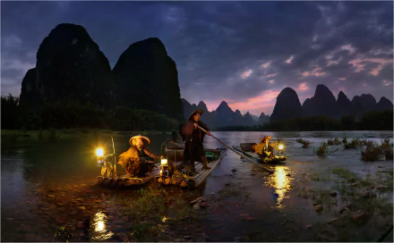 A serene depiction of fishermen on a river at dusk, surrounded by majestic mountains and soft lighting, captures the essence of traditional fishing culture in a stunning HD wallpaper.