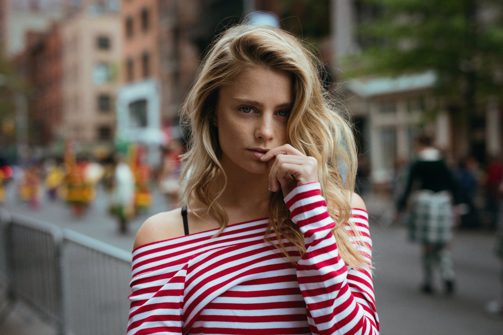 A blonde woman model poses stylishly in a striped off-shoulder top against an urban backdrop, captured in an HD desktop wallpaper and background setting.