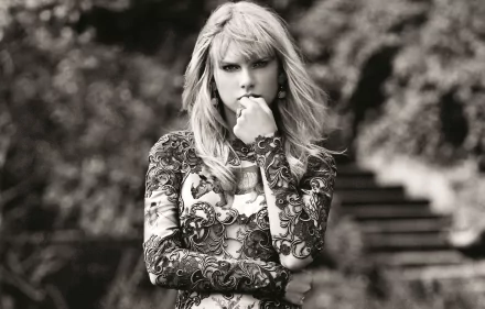 Black and white HD desktop wallpaper of American singer Taylor Swift with blonde hair, wearing a patterned long-sleeve top, posed thoughtfully outdoors.