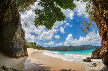 Tropical beach with clear blue ocean, white sand, and lush greenery framed by rocky cliffs under a bright, partly cloudy sky—vibrant HD desktop wallpaper.