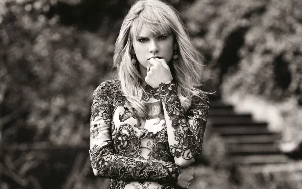 Black and white HD desktop wallpaper of American singer Taylor Swift with blonde hair, wearing a patterned long-sleeve top, posed thoughtfully outdoors.