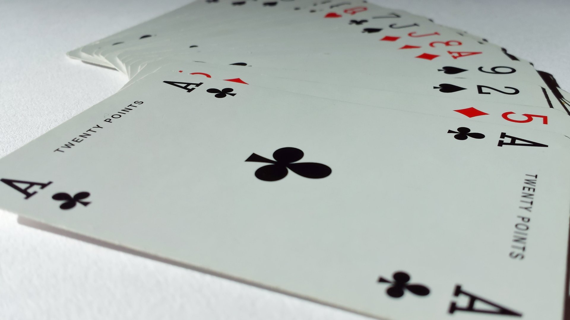 HD desktop wallpaper featuring a close-up of a man-made playing card spread, highlighting clubs, diamonds, and hearts suits on a clean white background.