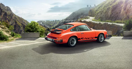 An orange Porsche 911 Carrera is parked on a winding road, surrounded by scenic hills, showcasing its sleek design against a stunning landscape backdrop.