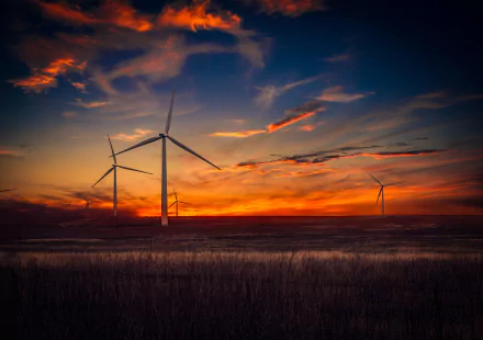 HD desktop wallpaper of an orange sunset landscape featuring a sky filled with clouds and several man-made wind turbines on the horizon.