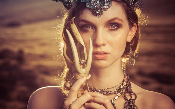 A close-up of a redheaded woman with green eyes, adorned in intricate jewelry and a striking necklace, holding an antler. She embodies a captivating cosplay aesthetic.