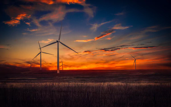 HD desktop wallpaper of an orange sunset landscape featuring a sky filled with clouds and several man-made wind turbines on the horizon.