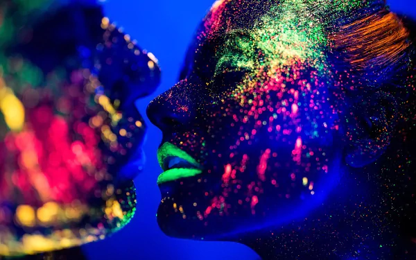 HD close-up photography of two faces and lips dusted with fluorescent neon paint glowing under blacklight, vivid PC desktop wallpaper background.